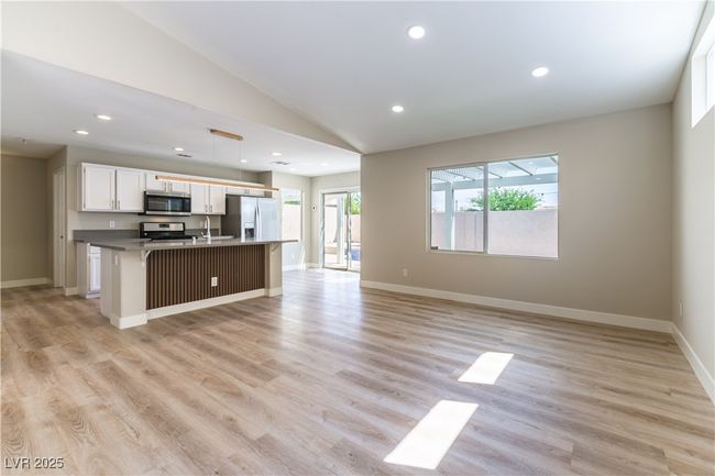 Kitchen with appliances with stainless steel finishes, lofted ceiling, open floor plan, a kitchen island with sink, and white cabinetry | Image 6