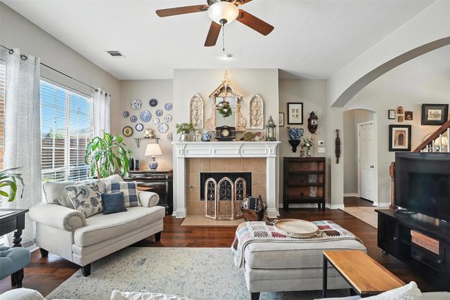 Living room with a ceiling fan, wood finished floors, arched walkways, and a tiled fireplace | Image 8