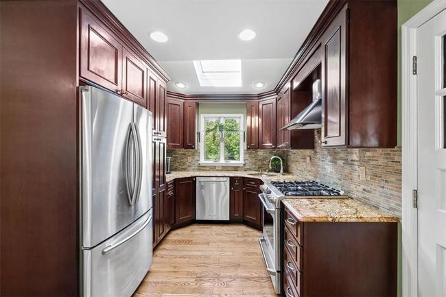 Kitchen with wall chimney range hood, light hardwood / wood-style floors, a skylight, stainless steel appliances, and backsplash | Image 6