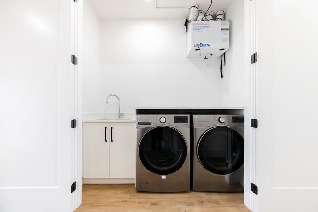 Laundry room with washer and clothes dryer, light wood-type flooring, cabinet space, and water heater | Image 27