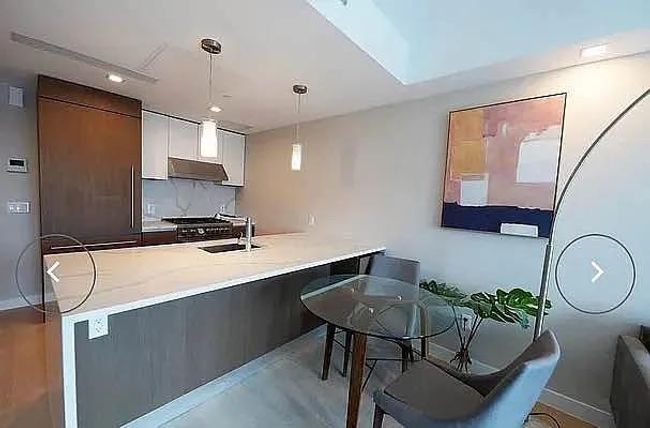 Kitchen with a sink, a peninsula, hanging light fixtures, under cabinet range hood, and light countertops | Image 9