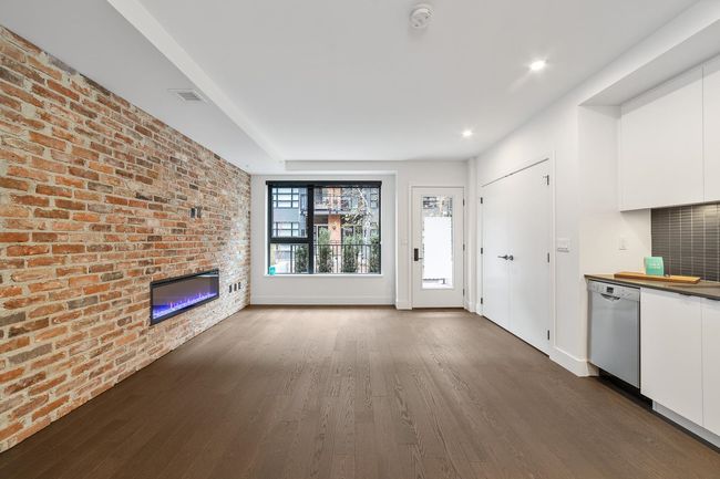 Unfurnished living room featuring dark wood-style floors, a fireplace, brick wall, and recessed lighting | Image 17