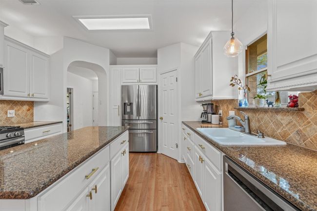 Kitchen with appliances with stainless steel finishes, arched walkways, white cabinets, decorative backsplash, and light wood-style floors | Image 12