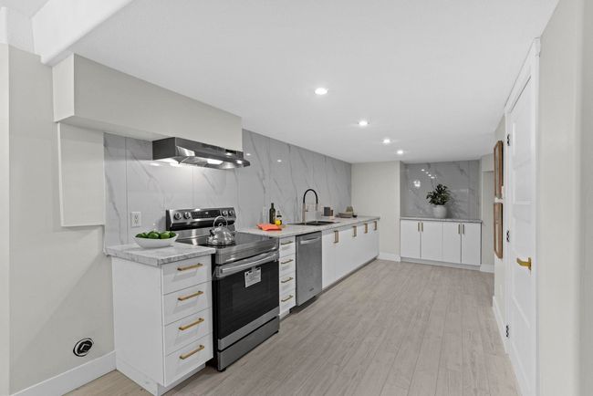 Kitchen featuring white cabinetry, recessed lighting, under cabinet range hood, a sink, and stainless steel appliances | Image 33