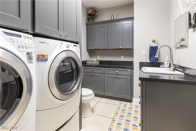 Laundry area with light tile patterned floors, a sink, and washer and dryer | Image 31
