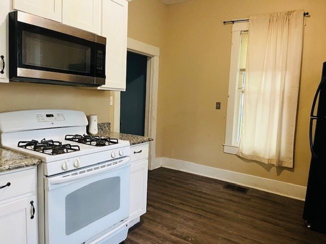 Kitchen with stainless steel microwave, white range with gas cooktop, baseboards, dark wood-style flooring, and freestanding refrigerator | Image 14