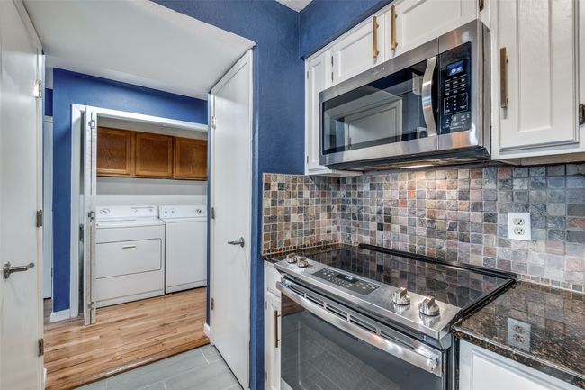 Kitchen with appliances with stainless steel finishes, washer and clothes dryer, white cabinetry, dark stone counters, and backsplash | Image 7