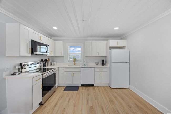 Kitchen with white appliances, a sink, crown molding, white cabinets, and light wood-type flooring | Image 28