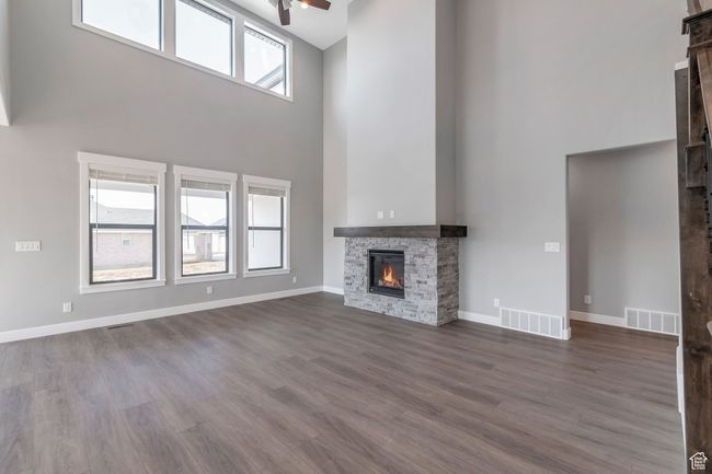 Unfurnished living room with a towering ceiling, a fireplace, a ceiling fan, and dark wood-type flooring | Image 12