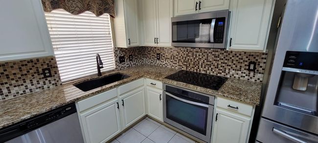 Kitchen with appliances with stainless steel finishes, backsplash, white cabinetry, and stone counters | Image 5