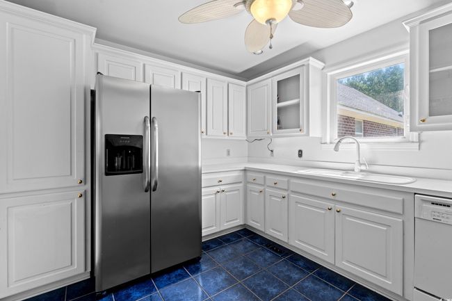 Kitchen featuring stainless steel refrigerator with ice dispenser, white dishwasher, dark tile patterned floors, glass insert cabinets, and white cabinets | Image 4