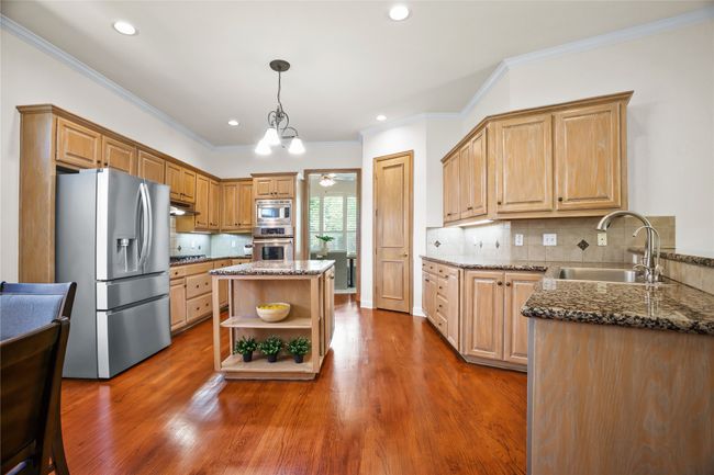 Kitchen featuring appliances with stainless steel finishes, open shelves, dark stone counters, dark wood-type flooring, and ornamental molding | Image 7
