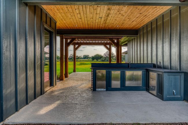 Outdoor summer kitchen with sleek countertops, stainless steel appliances, and a charming wooden ceiling, perfect for entertaining and enjoying beautiful views. | Image 34
