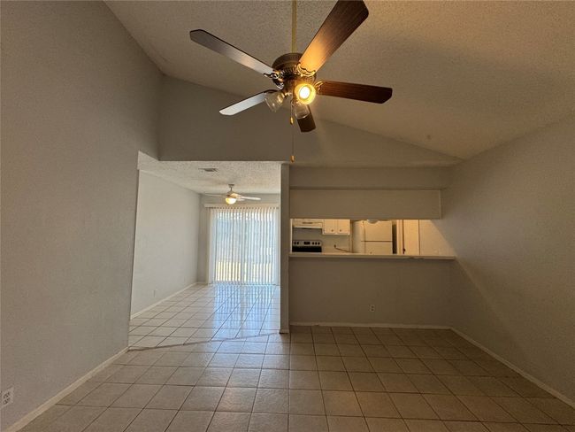 Spare room featuring a textured ceiling, vaulted ceiling, light tile patterned floors, and a ceiling fan | Image 4