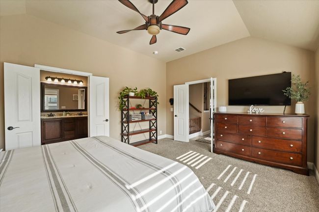 Carpeted bedroom featuring connected bathroom, ceiling fan, baseboards, lofted ceiling, and visible vents | Image 21