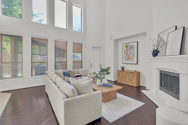 Living room with plenty of natural light, a towering ceiling, dark wood-style floors, and a fireplace with raised hearth | Image 10