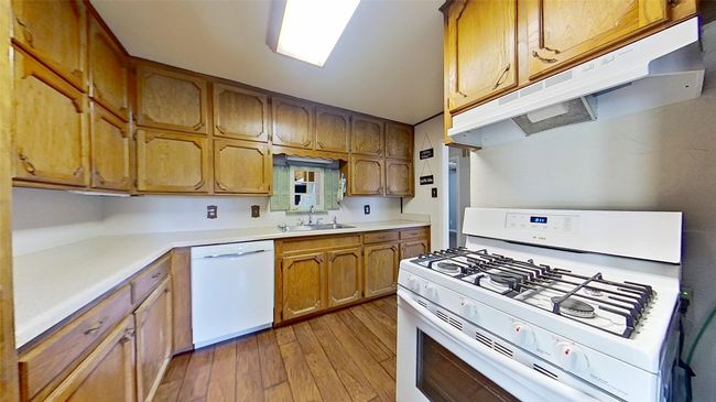 Kitchen with white appliances, under cabinet range hood, a sink, light wood-style flooring, and brown cabinets | Image 10