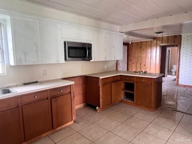 Kitchen featuring stainless steel microwave, light countertops, light tile patterned floors, brown cabinetry, and wood walls | Image 12