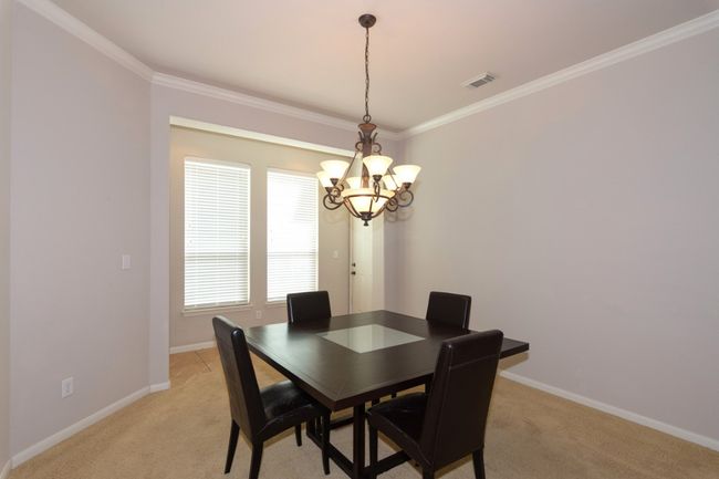 Dining space featuring visible vents, baseboards, an inviting chandelier, ornamental molding, and light carpet | Image 8