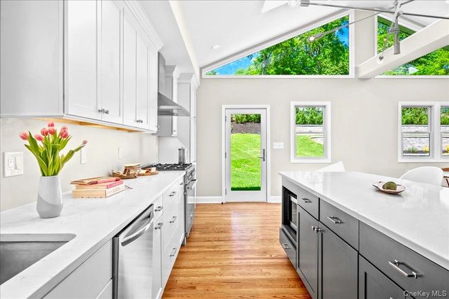 Kitchen with appliances with stainless steel finishes, white cabinetry, light wood-style floors, baseboards, and a sink | Image 13