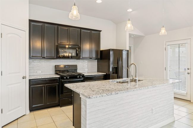 Kitchen with light tile patterned flooring, vaulted ceiling, a sink, black appliances, and decorative light fixtures | Image 12