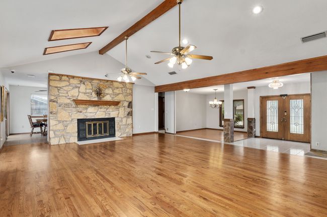 Unfurnished living room featuring ceiling fan with notable chandelier, visible vents, a wealth of natural light, and a stone fireplace | Image 14