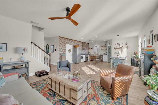 Living room with baseboards, visible vents, brick wall, light wood-style flooring, and stairs open to the dining and kitchen | Image 8