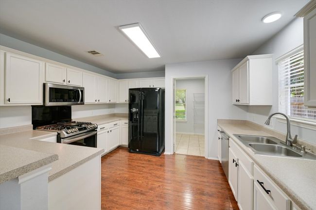 Kitchen featuring appliances with stainless steel finishes, white cabinets, light countertops, and dark wood finished floors | Image 6