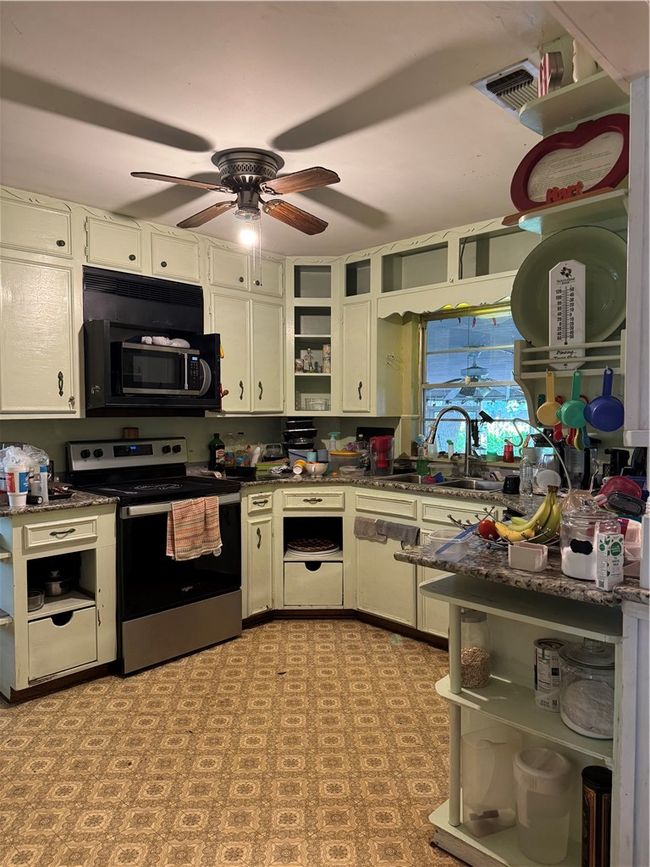 Kitchen featuring stove, open shelves, a ceiling fan, a sink, and dark countertops | Image 5