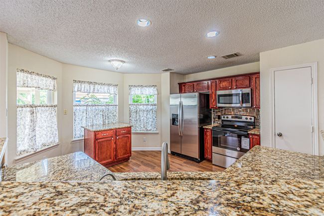 Kitchen featuring appliances with stainless steel finishes, wood finished floors, a textured ceiling, backsplash, and reddish brown cabinets | Image 11