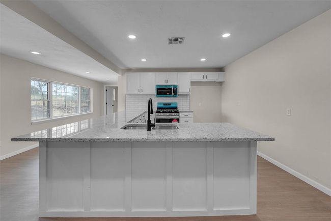 Kitchen featuring light hardwood / wood-style flooring, tasteful backsplash, white cabinets, light stone counters, and appliances with stainless steel finishes | Image 19