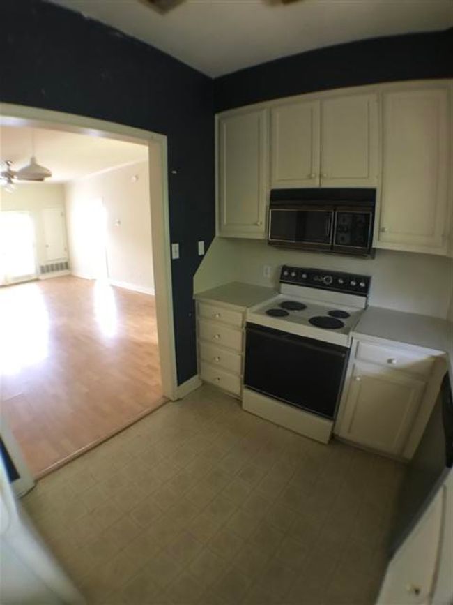 Kitchen featuring a ceiling fan, black microwave, light floors, white electric range, and white cabinetry | Image 11