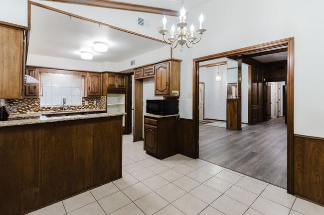 Kitchen featuring black microwave, light tile patterned flooring, a notable chandelier, and a sink | Image 12