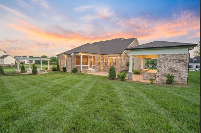 Sunset views, lush green space, & the ultimate backyard setup—featuring a screened porch, luxury outdoor kitchen w/remote-control shade, & a dreamy pergola w/swing & waterfall backdrop.This is outdoor living at its finest! | Image 10