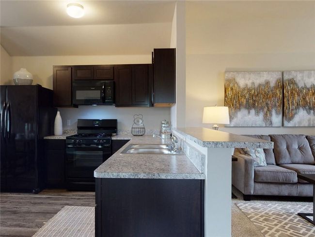 Kitchen with black appliances, kitchen peninsula, sink, hardwood / wood-style flooring, and dark brown cabinetry | Image 7