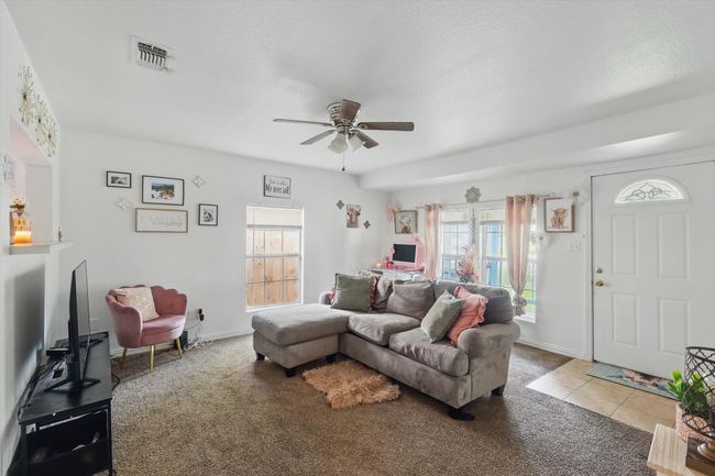 Living area with carpet floors, ceiling fan, a wealth of natural light, and visible vents | Image 6