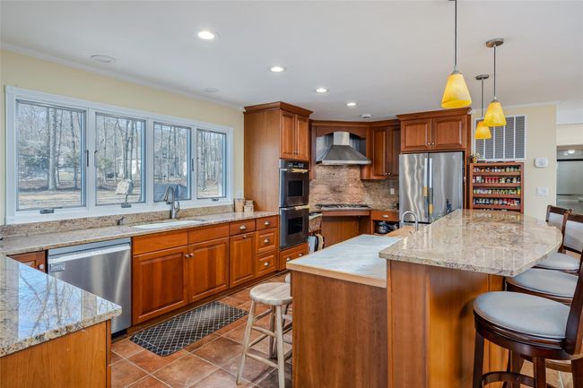 Kitchen featuring a sink, appliances with stainless steel finishes, a kitchen bar, tile patterned floors, and wall chimney range hood | Image 13