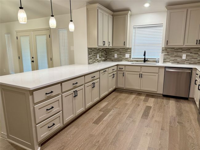 Kitchen with stainless steel dishwasher, a peninsula, light wood-type flooring, tasteful backsplash, and light countertops | Image 7