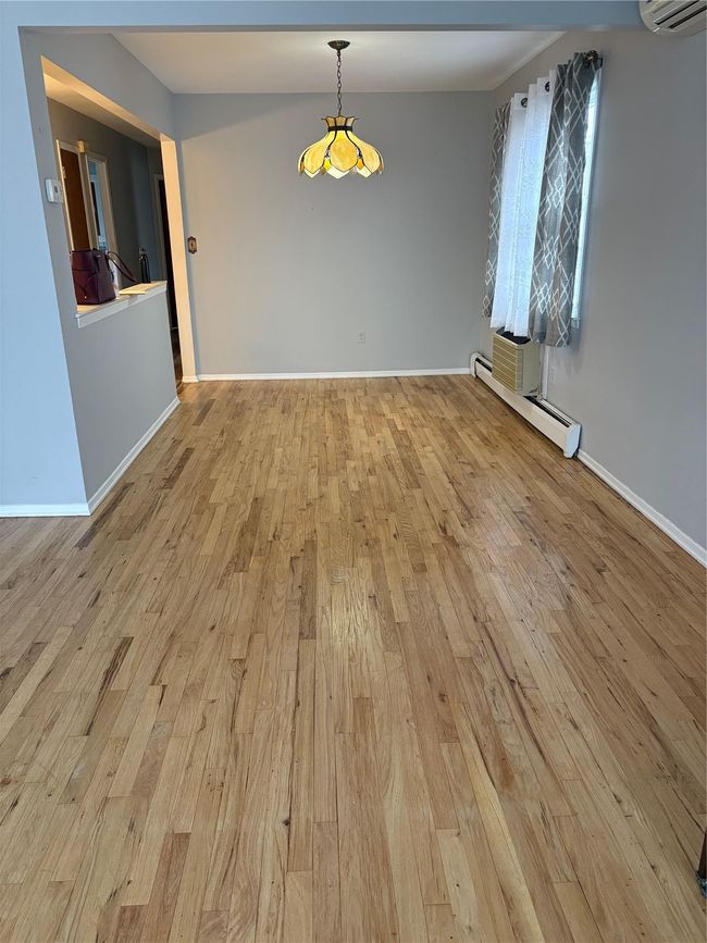 Unfurnished dining area featuring baseboards, light wood-type flooring, a wall unit AC, and baseboard heating | Image 4