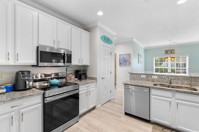 Kitchen with appliances with stainless steel finishes, a sink, crown molding, white cabinetry, and light wood-style flooring | Image 4