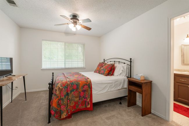 Primary Bedroom featuring light carpet, multiple windows, a textured ceiling, ensuite bathroom, and a ceiling fan | Image 18