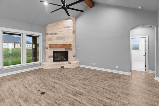 Unfurnished living room with a ceiling fan, arched walkways, beam ceiling, wood finished floors, and a fireplace | Image 8