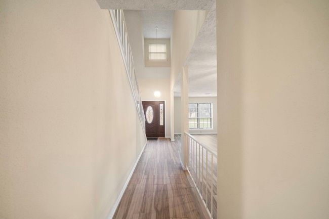 Step inside to a welcoming foyer highlighted by soaring ceilings and neutral tile flooring. The entry offers a direct view of the open living area and features a modern stair railing. | Image 7