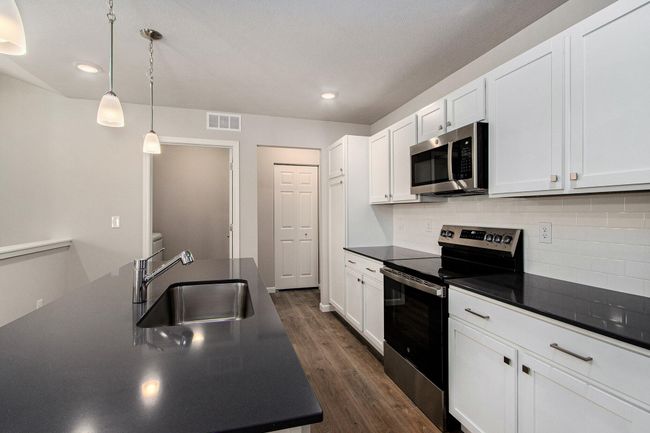 Bright, white kitchen cabinetry is accented by white quartz counters and tile backsplash. The kitchen island provides prep and sitting space and is accented by pendant lighting above. Stainless steel appliances are included! | Image 4