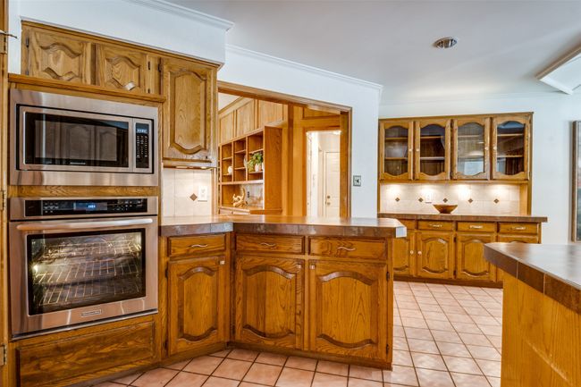 Kitchen with stainless steel appliances, crown molding, decorative backsplash, brown cabinetry, and light tile patterned flooring | Image 9