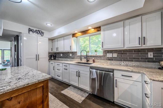 Kitchen with stainless steel dishwasher, dark wood-type flooring, white cabinets, backsplash, and light stone countertops | Image 23