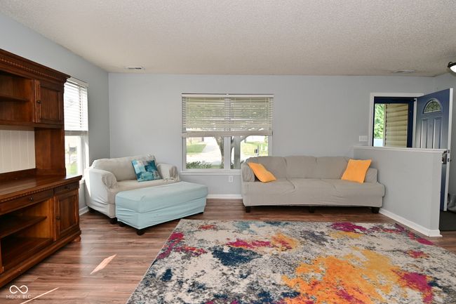 living area with a textured ceiling, healthy amount of natural light, wood finished floors, and baseboards | Image 6