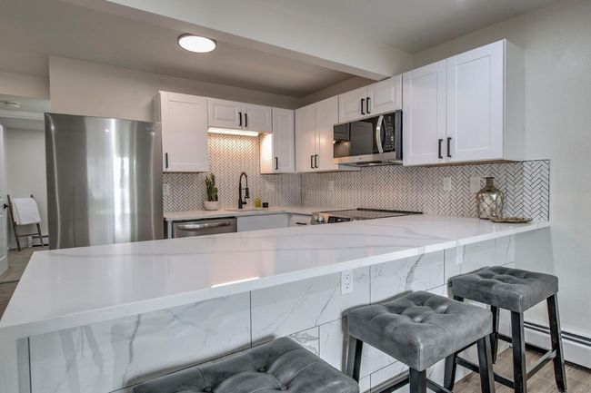 Kitchen featuring backsplash, a peninsula, appliances with stainless steel finishes, and white cabinetry | Image 12