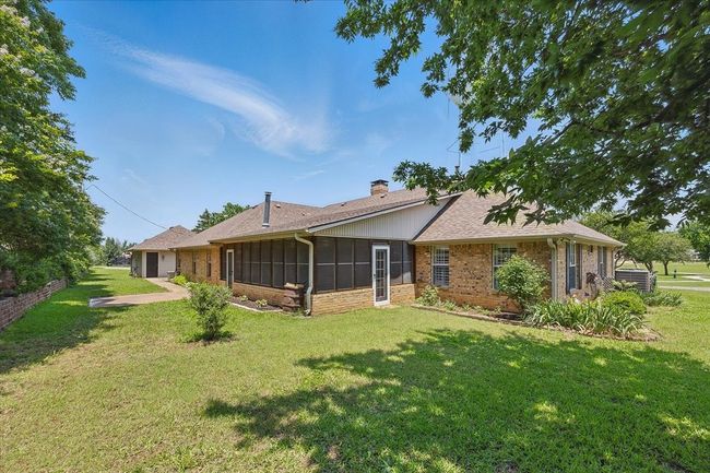 Rear view of house with a chimney, brick siding, a sunroom, a lawn, and a shingled roof | Image 25