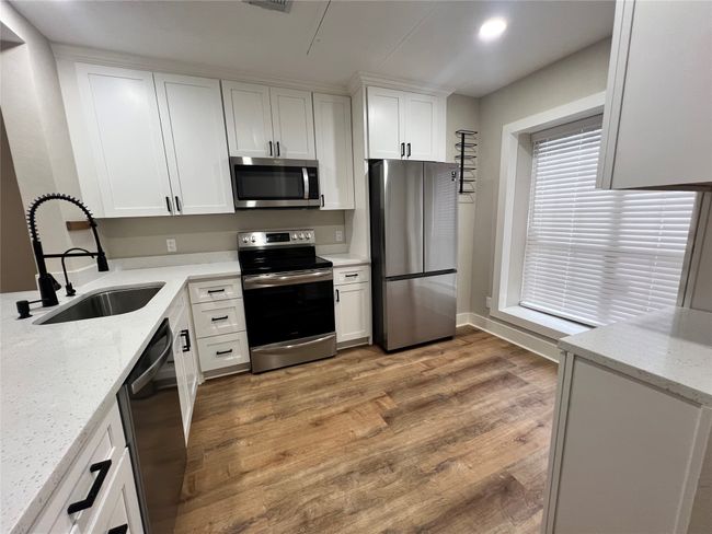 Kitchen featuring stainless steel appliances, a sink, white cabinets, light wood-style floors, and light stone countertops | Image 11